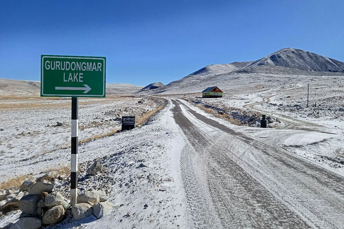 The snow-lined road towards Gurudongmar Lake with a roadside signboard